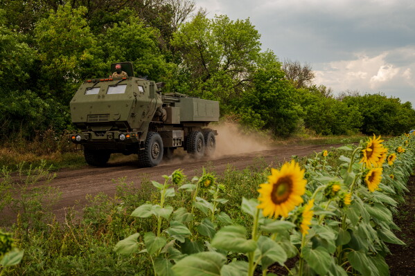 Член українського екіпажу HIMARS, прикріпленого до 148-ї бригади, дивиться на машину, що їде вздовж лінії фронту на сході України, прямуючи, щоб обстріляти ракети по російських позиціях, субота, 8 серпня 2026 р. (AP Photo/Dan Bashakov)