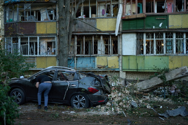 Місцевий житель дивиться всередину зруйнованого автомобіля поруч із сильно пошкодженими житловими будинками після нічної російської атаки в Києві, Україна, четвер, 20 серпня 2026 р. (AP Photo/Francisco Seco)